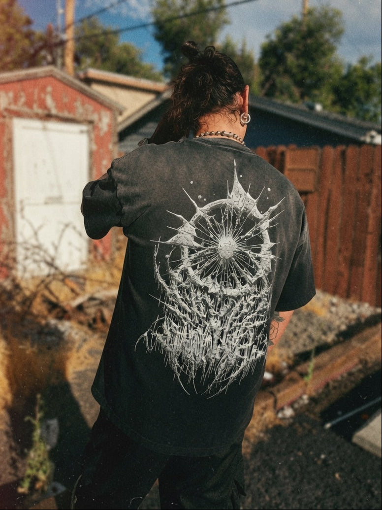 A person viewed from behind wearing a faded black t-shirt with a large white spiderweb graphic on the back, standing outdoors in a backyard setting.
