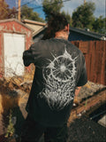 A person viewed from behind wearing a faded black t-shirt with a large white spiderweb graphic on the back, standing outdoors in a backyard setting.